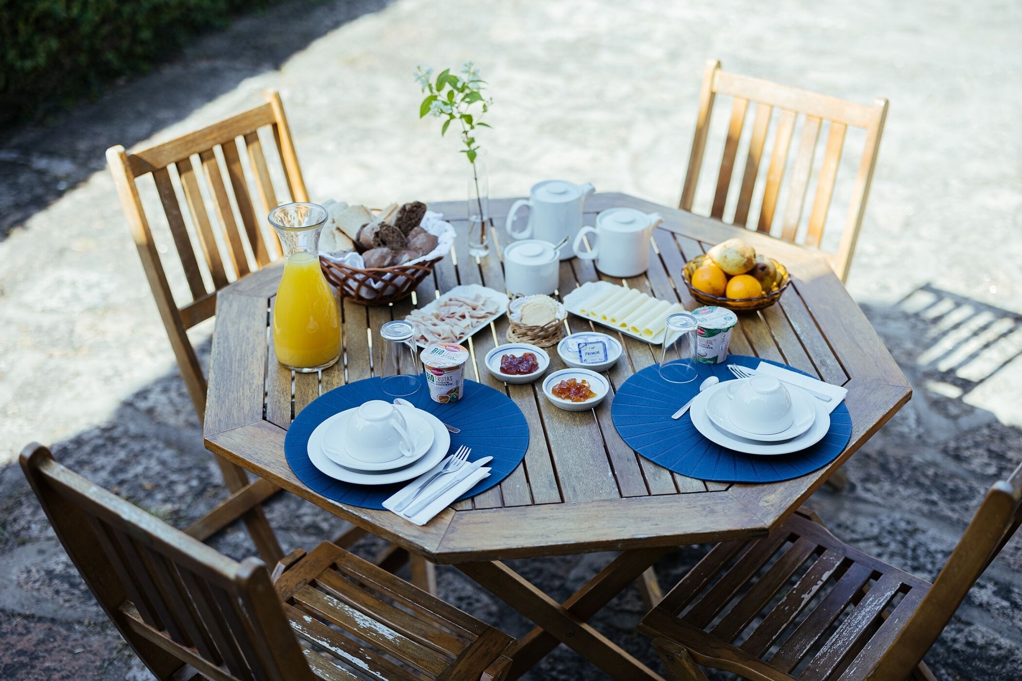 Mesa de madeira posta para o café da manhã, com pratos, xícaras e uma tigela de frutas.