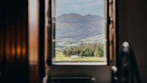 A view through an open door of a room with a window overlooking a rural landscape with mountains and a small building.
