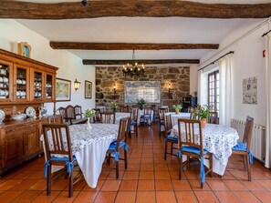 A dining area with wooden tables and chairs, a stone wall, and a wooden cabinet with dishes. - Quinta Stº António | Quinteiro | Monção | Rural Tourism | Pool (Monção)