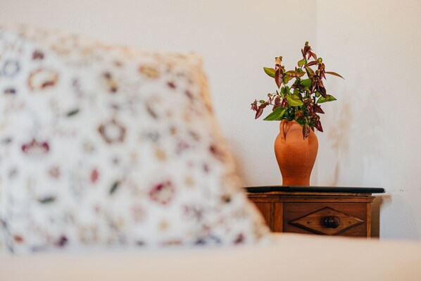 A room with a patterned pillow, a wooden nightstand, and a terracotta vase with a plant. - Quinta Stº António | Quinteiro | Monção | Rural Tourism | Pool (Monção)