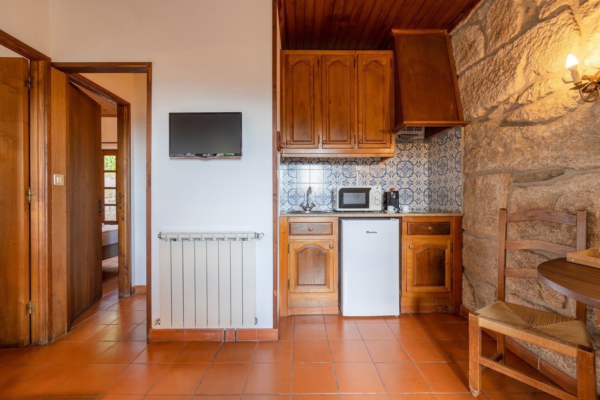 Una cocina compacta con armarios de madera, un refrigerador blanco, un microondas y una pared de piedra.