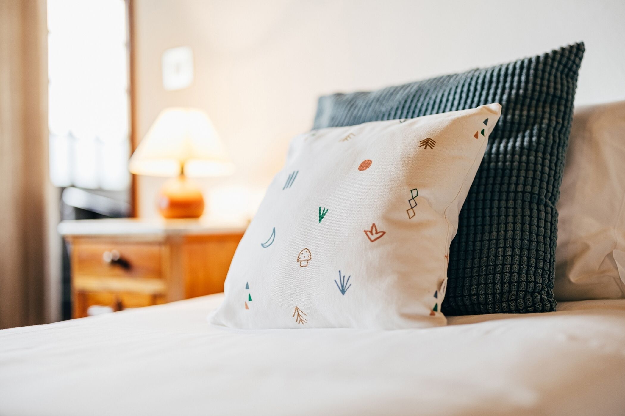 Una cama con un cojín blanco de diseños coloridos y un cojín verde oscuro.