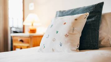 Una cama con un cojín blanco de diseños coloridos y un cojín verde oscuro.