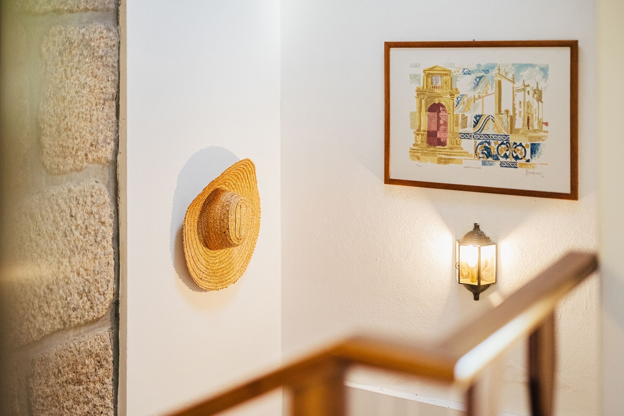 Una pared con una obra de arte enmarcada, una lámpara de pared y un sombrero de paja.