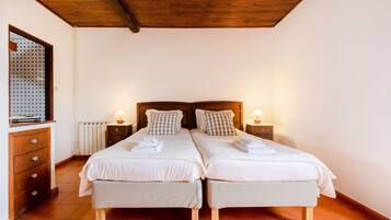 Habitación doble con dos camas, cabeceros de madera, mesitas de noche con lámparas, cómoda de madera y radiador.