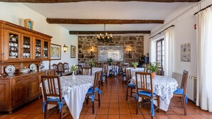 A dining area with wooden tables and chairs, a stone wall, and a wooden cabinet with dishes. - Quinta Stº António | Palheiro B | Monção | Rural Tourism | Pool (Monção)