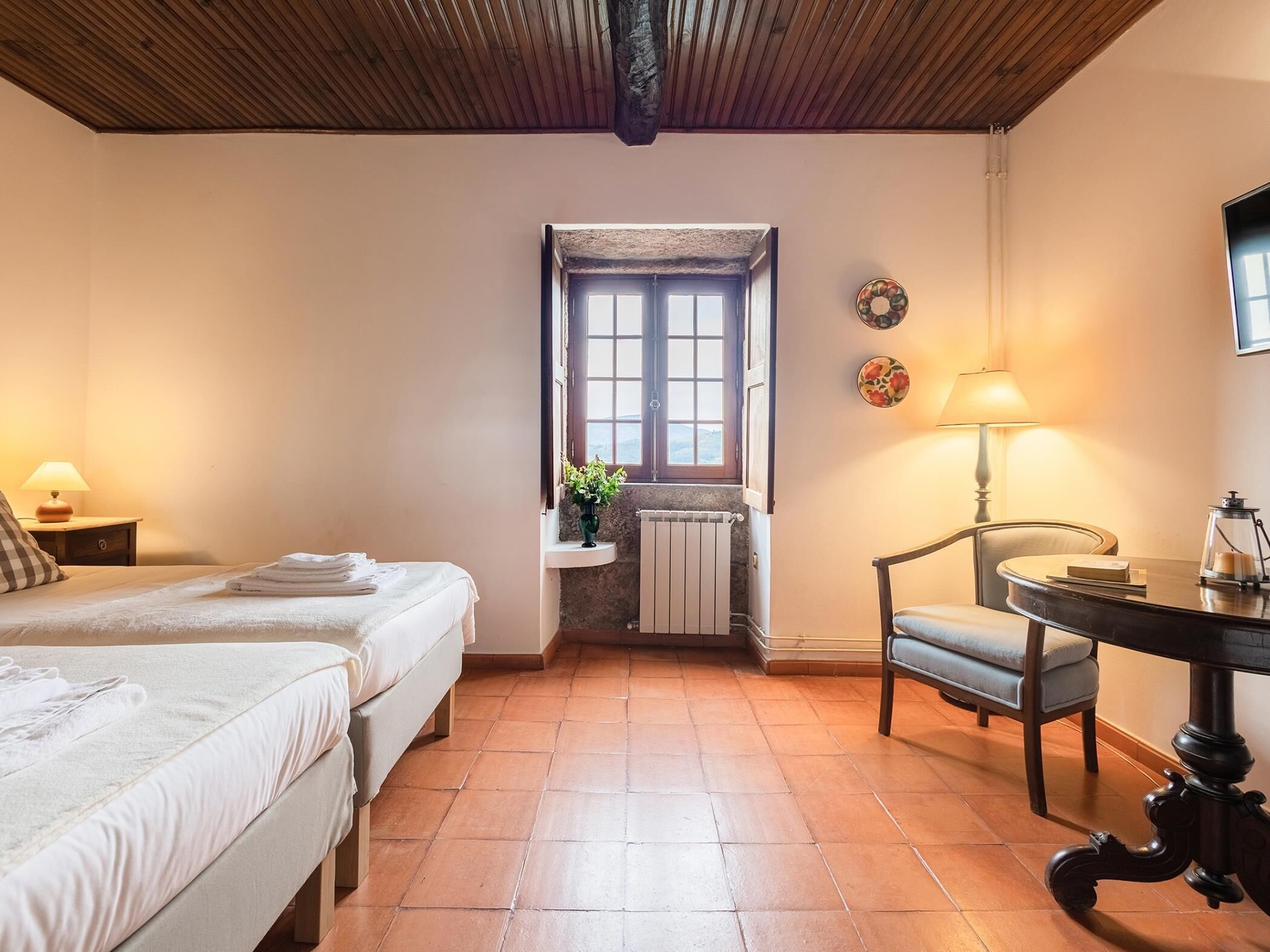 Ein gemütliches Zimmer mit zwei Betten, einem Tisch, einem Stuhl, einem Fenster mit Blick und einer Heizung.
