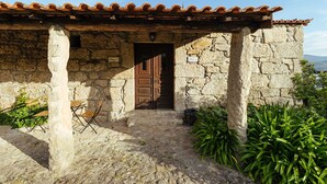 A stone building with a tiled roof, a wooden door, and a small outdoor seating area with chairs. - Quinta Stº António | Palheiro B | Monção | Rural Tourism | Pool (Monção)