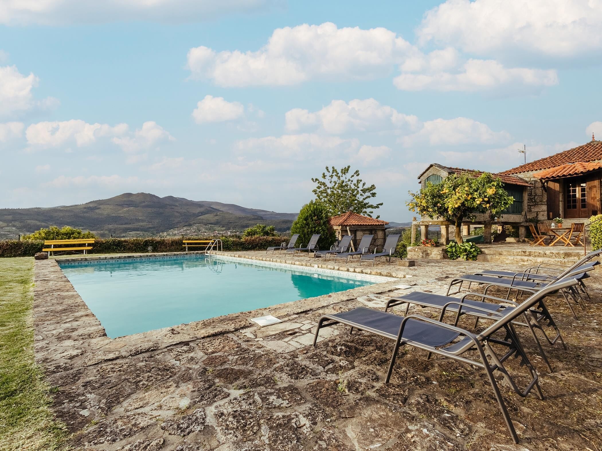 A swimming pool with lounge chairs, a stone patio, and a view of mountains.
