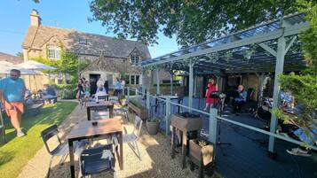 An outdoor patio area with tables and chairs, a covered stage, and a stone building in the background.