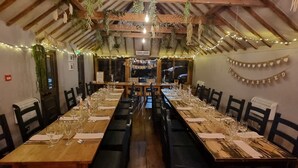 Una larga mesa de comedor de madera dispuesta con múltiples sillas, luces de guirnalda y un cartel que dice 'recién casados'.