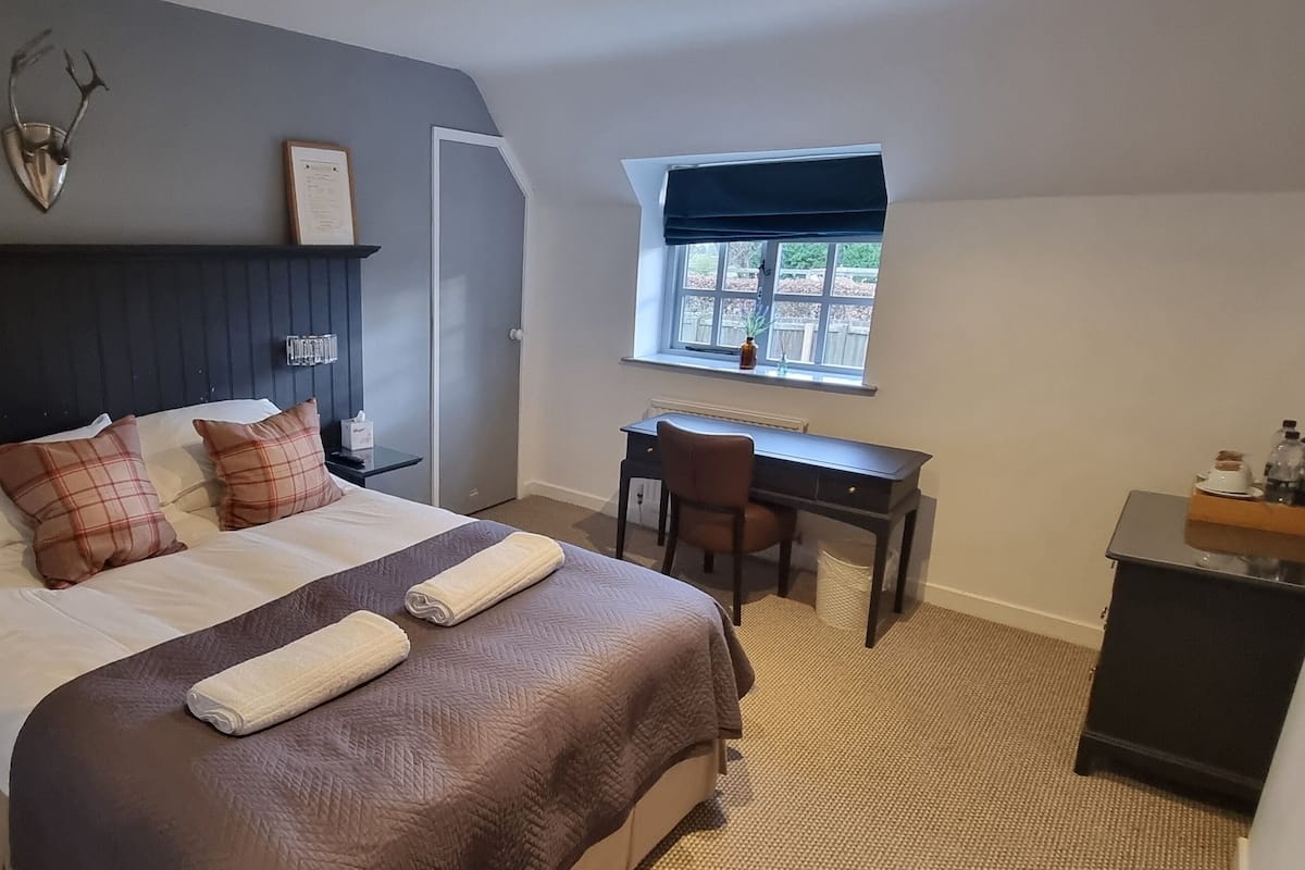 Una habitación de hotel con una cama grande, un escritorio, una silla, un teléfono y una ventana con vistas.