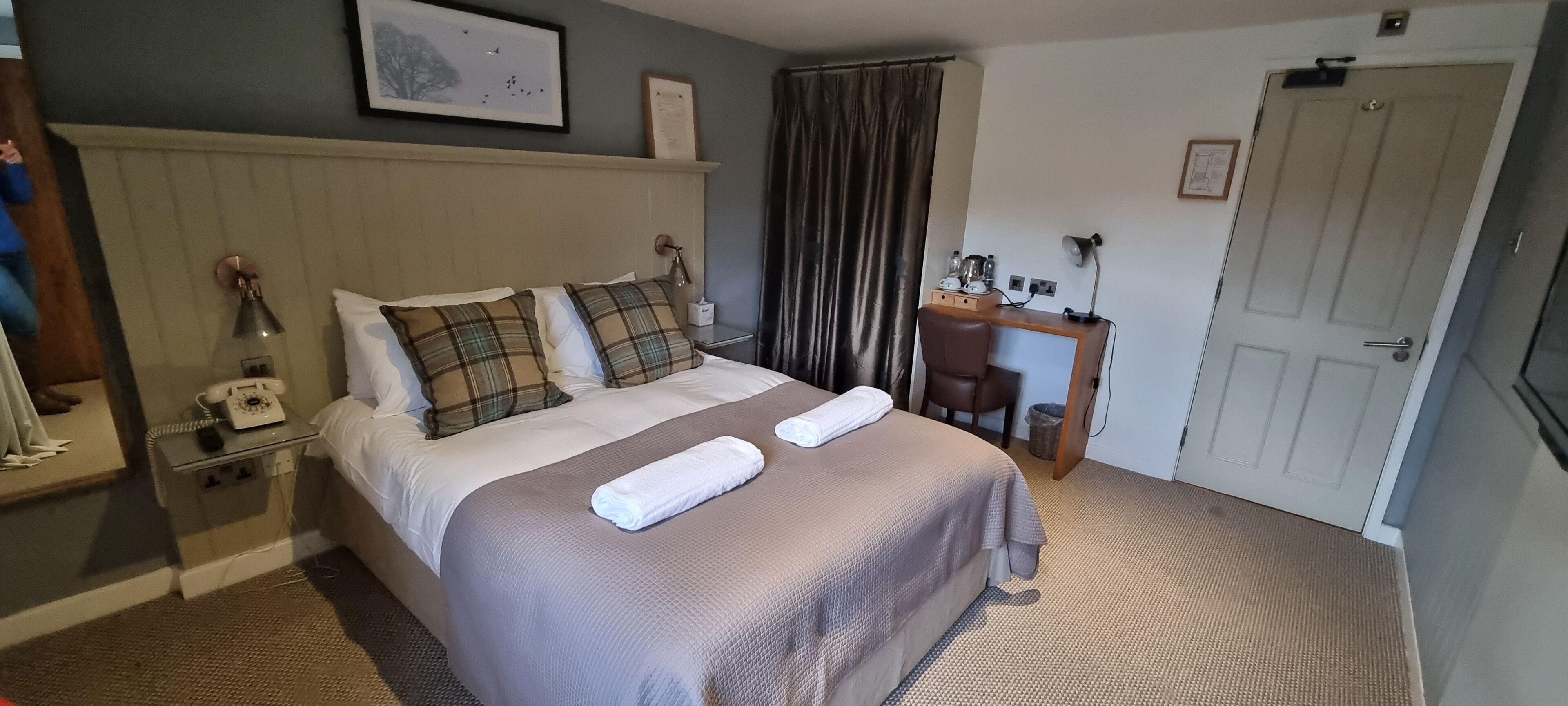 A neatly arranged hotel room with a bed, bedside table, lamp, and a desk with a chair.