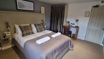 A neatly arranged hotel room with a bed, bedside table, lamp, and a desk with a chair.