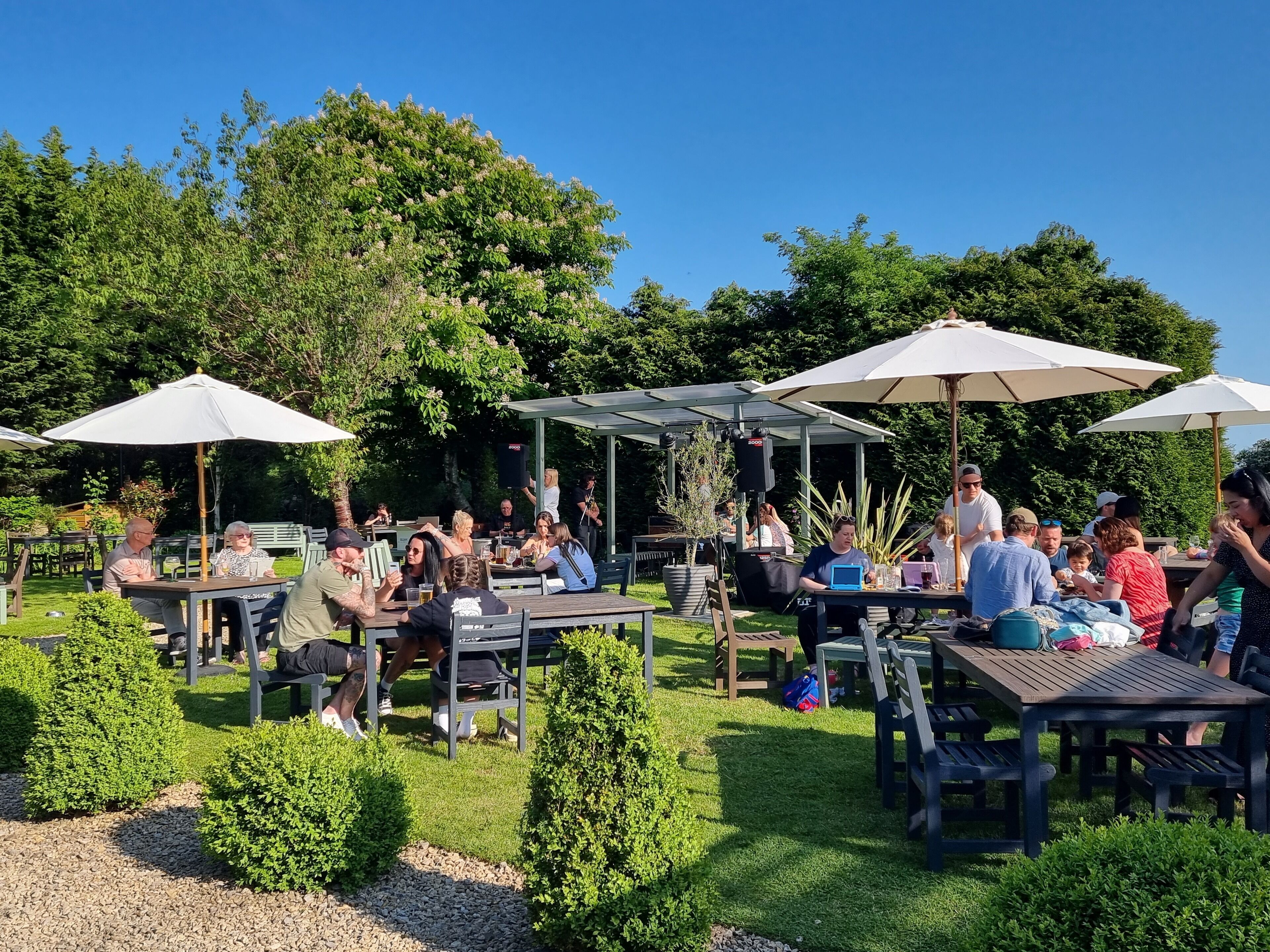 An outdoor seating area with tables and umbrellas, surrounded by greenery and trees.