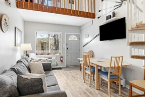 A modern living room with a sofa, dining table, chairs, a TV, and a staircase. - Play & Stay, Bergrand (mancelona)