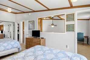A bedroom with two beds, a dresser, a television, a ceiling fan, and a wall-mounted shelf with decorative items.