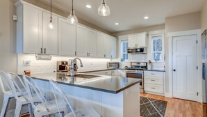 A modern kitchen with white cabinets, a large island with bar stools, a built-in oven, and pendant lighting.