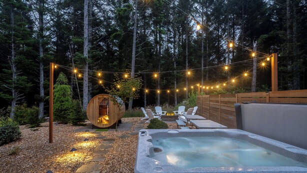 A hot tub with lounge chairs and a wooden barrel structure in a forested outdoor area.