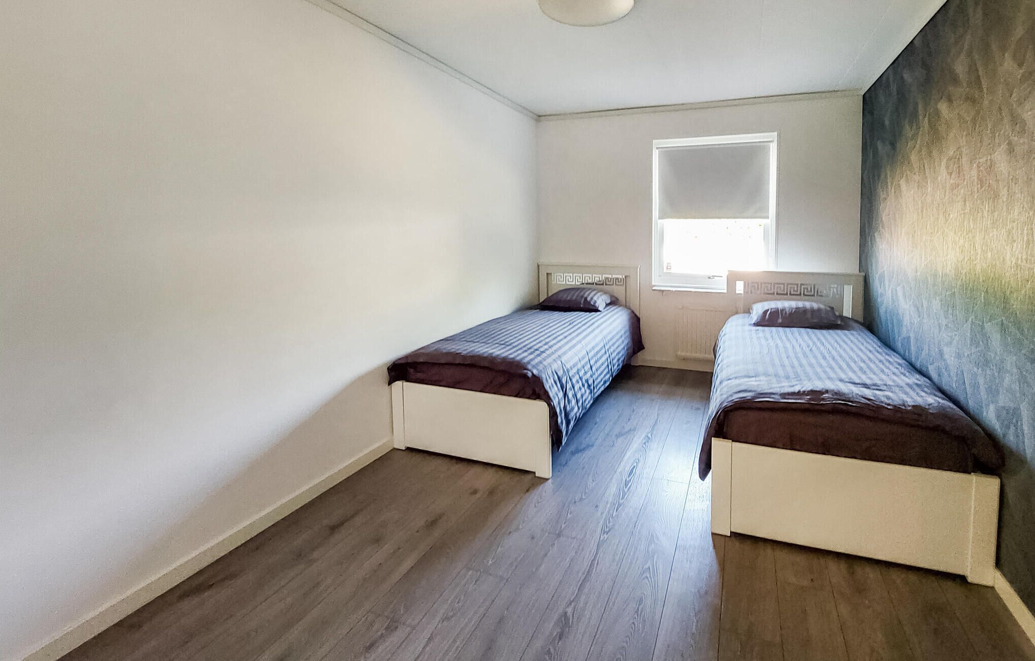Een kleine, schone kamer met twee enkele bedden, een raam en een effen witte muur.