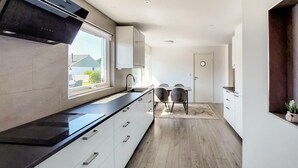 A modern kitchen with a black countertop, white cabinets, and a window overlooking a residential area. - Nice home in Helsingborg (Helsingborg)