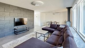 A modern living room with a stone wall, a flat-screen TV, a sectional sofa, a coffee table, and a large window with a view. - Nice home in Helsingborg (Helsingborg)