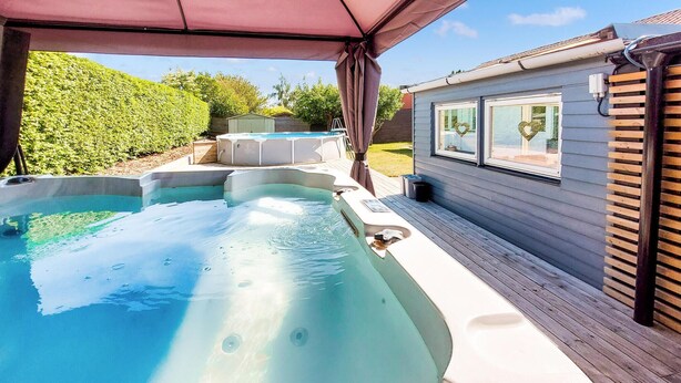 A hot tub area with a covered deck, a wooden deck, and a house with windows. - Nice home in Helsingborg (Helsingborg)