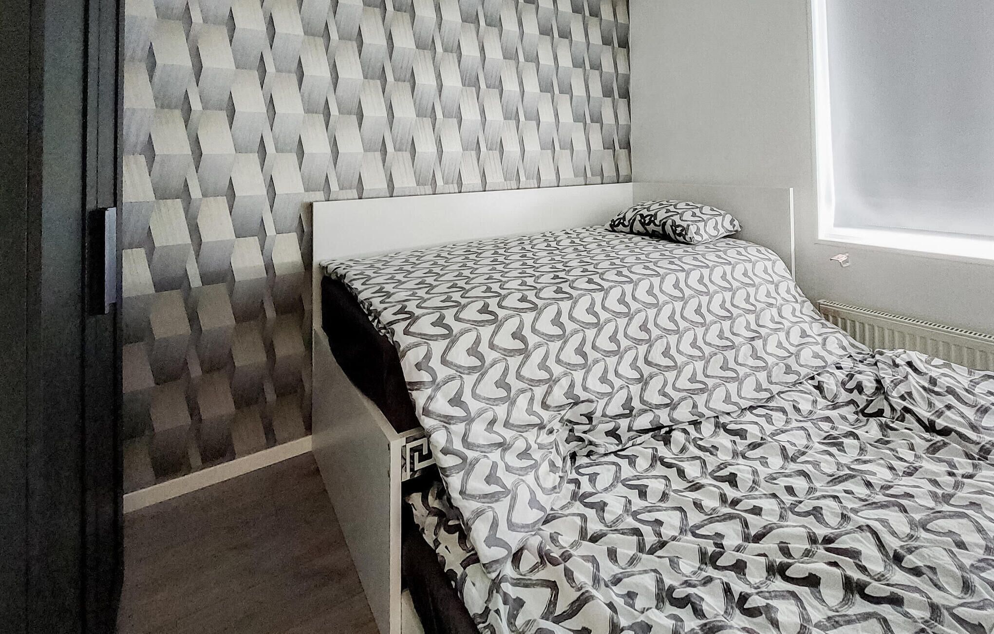 Une chambre à coucher avec une couvre-lit à motifs, une tête de lit blanche et un mur orné d’un motif géométrique.