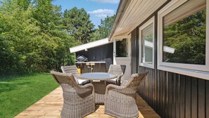 A deck with wicker furniture and a grill, surrounded by a wooden deck and a view of trees. - Beautiful home in Sejerø with kitchen (Sejerø)