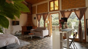 A cozy room with a sofa, a small table, and a TV. There's a fireplace, a window with curtains, and a view of greenery outside. - Cabaña El Encino en Real del Monte (Mineral del Monte)