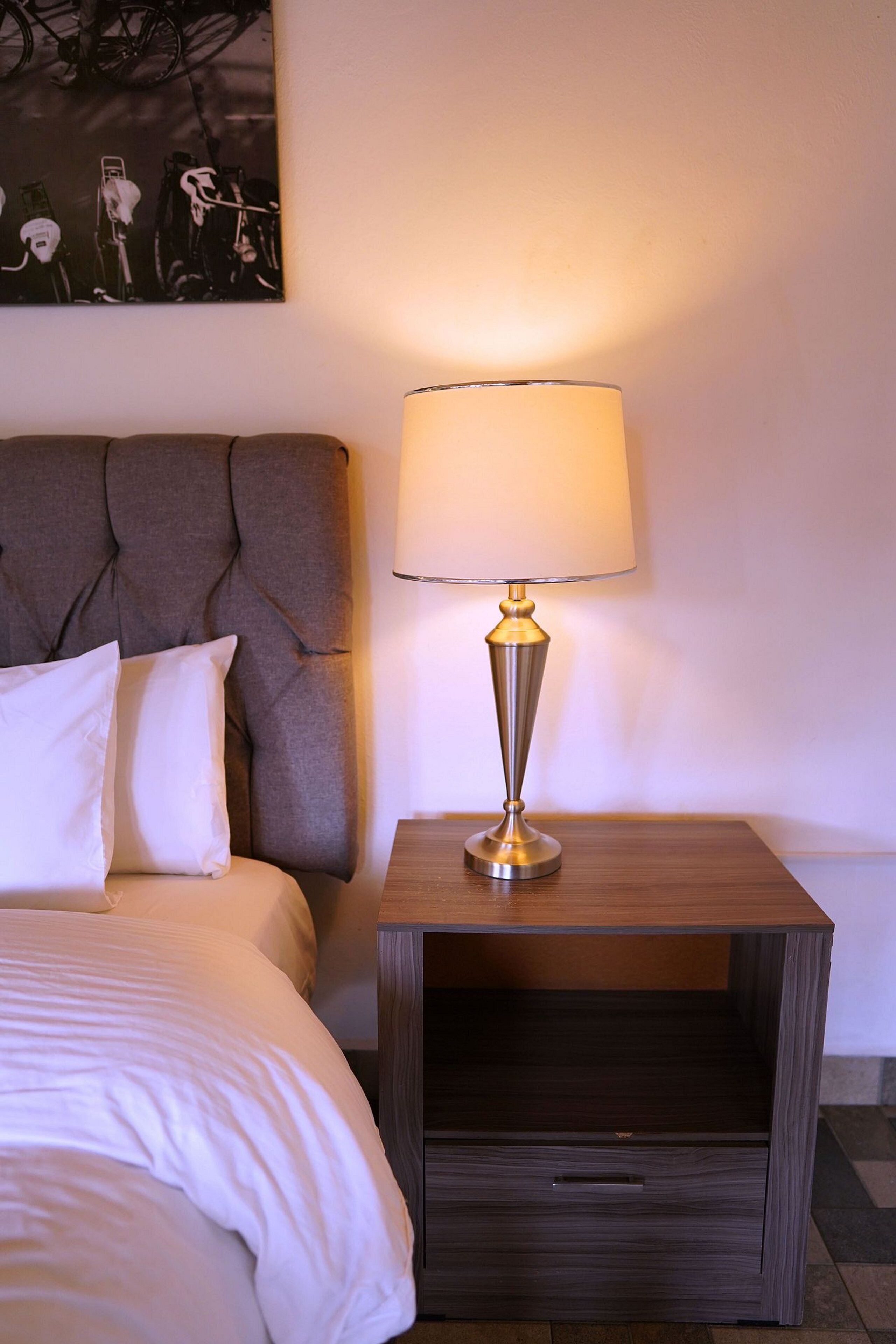 A neatly made bed with white linens, a tufted headboard, and a bedside table with a lamp.