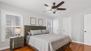 Un dormitorio con una cama, mesitas de noche, un ventilador de techo y dos cuadros en la pared.