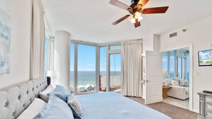 Un dormitorio amplio con una cama grande, un ventilador de techo y vistas al océano a través de ventanas amplias.