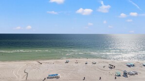 Ein Strand mit blauem Himmel, ruhiger See und mehreren Strandsonnen- und Zeltschirmen.