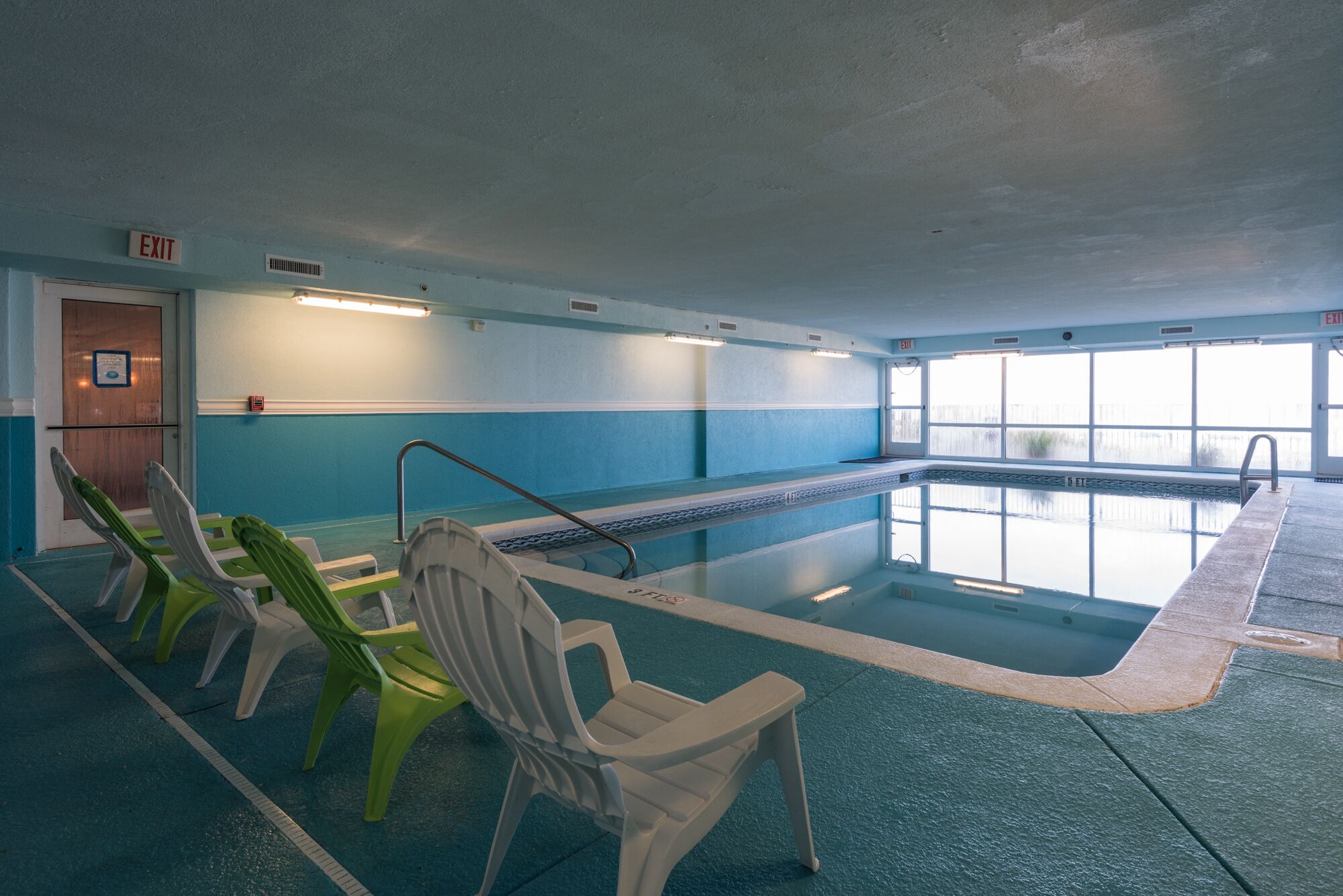 Une piscine intérieure avec des couloirs clairement délimités, un poste de surveillance pour le sauveteur et un panneau indiquant la sortie.