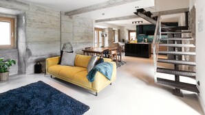 Un salon moderne avec un canapé jaune, un tapis bleu et un escalier menant à un niveau supérieur.