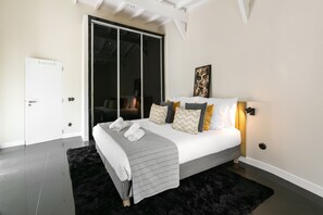A modern bedroom with a large bed, a black furry rug, a sliding door, and a wall-mounted light fixture.