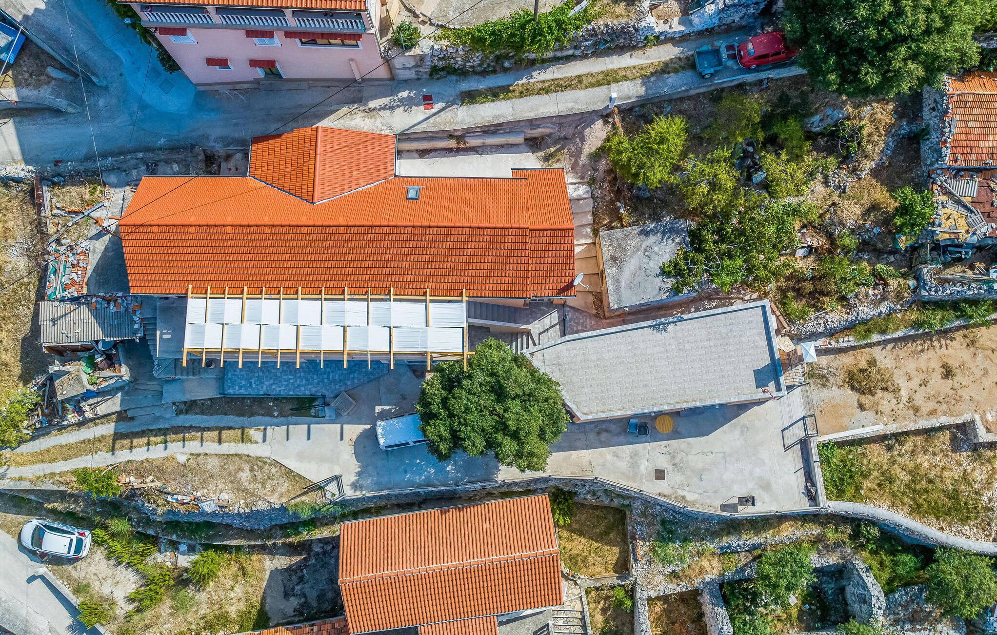 Vista aerea di un edificio con tetto in tegole rosse, piscina e area di parcheggio.