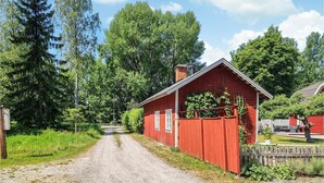 Punainen puinen rakennus, jonka luo johtaa kivituhkapolku. Rakennuksen ympärillä on vehreää kasvillisuutta ja puita.
