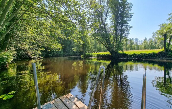 A calm river with a wooden dock extending into the water, surrounded by lush greenery and trees.