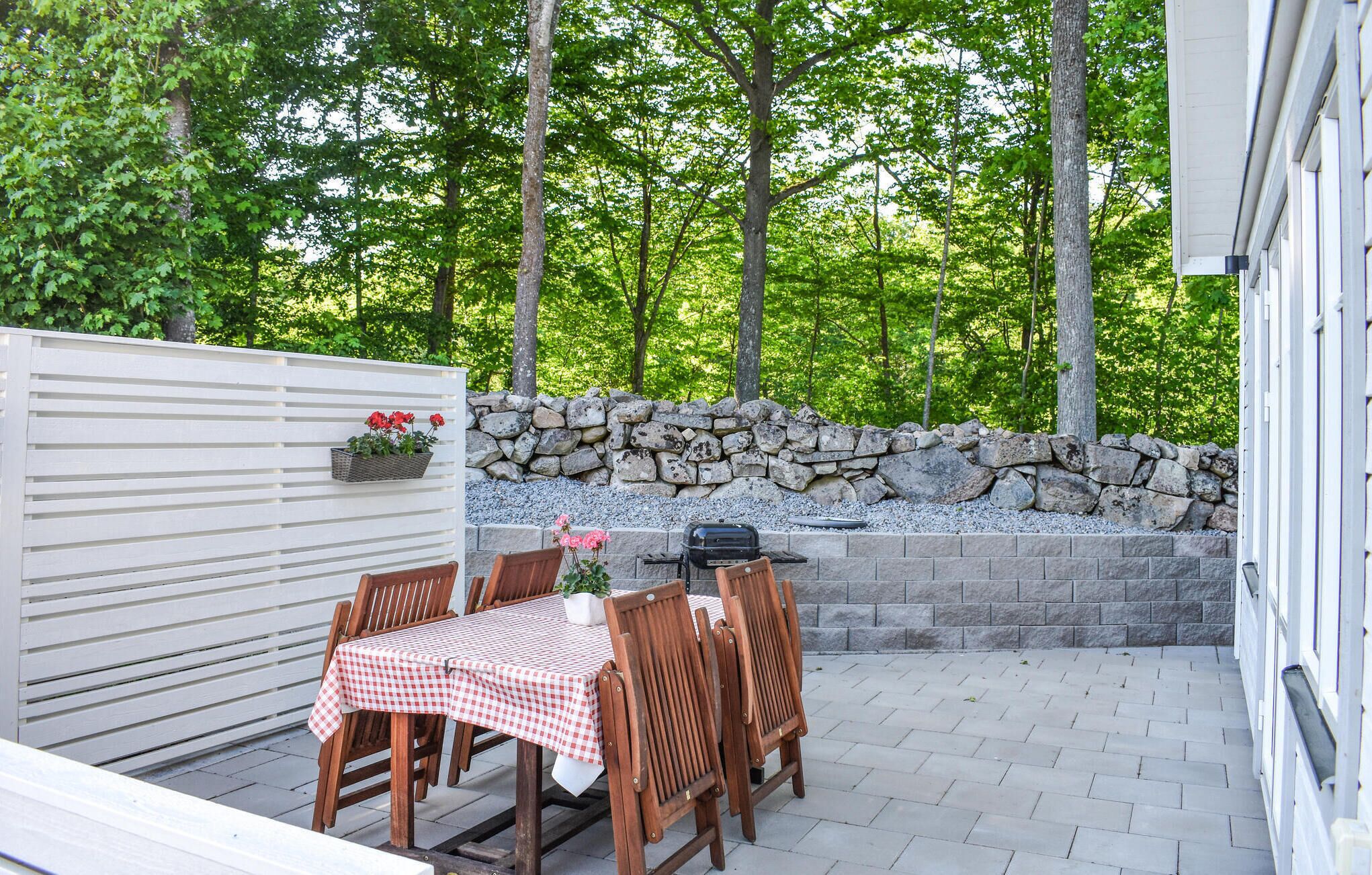 An outdoor patio with a table and chairs, a barbecue grill, a stone wall, and a white fence.
