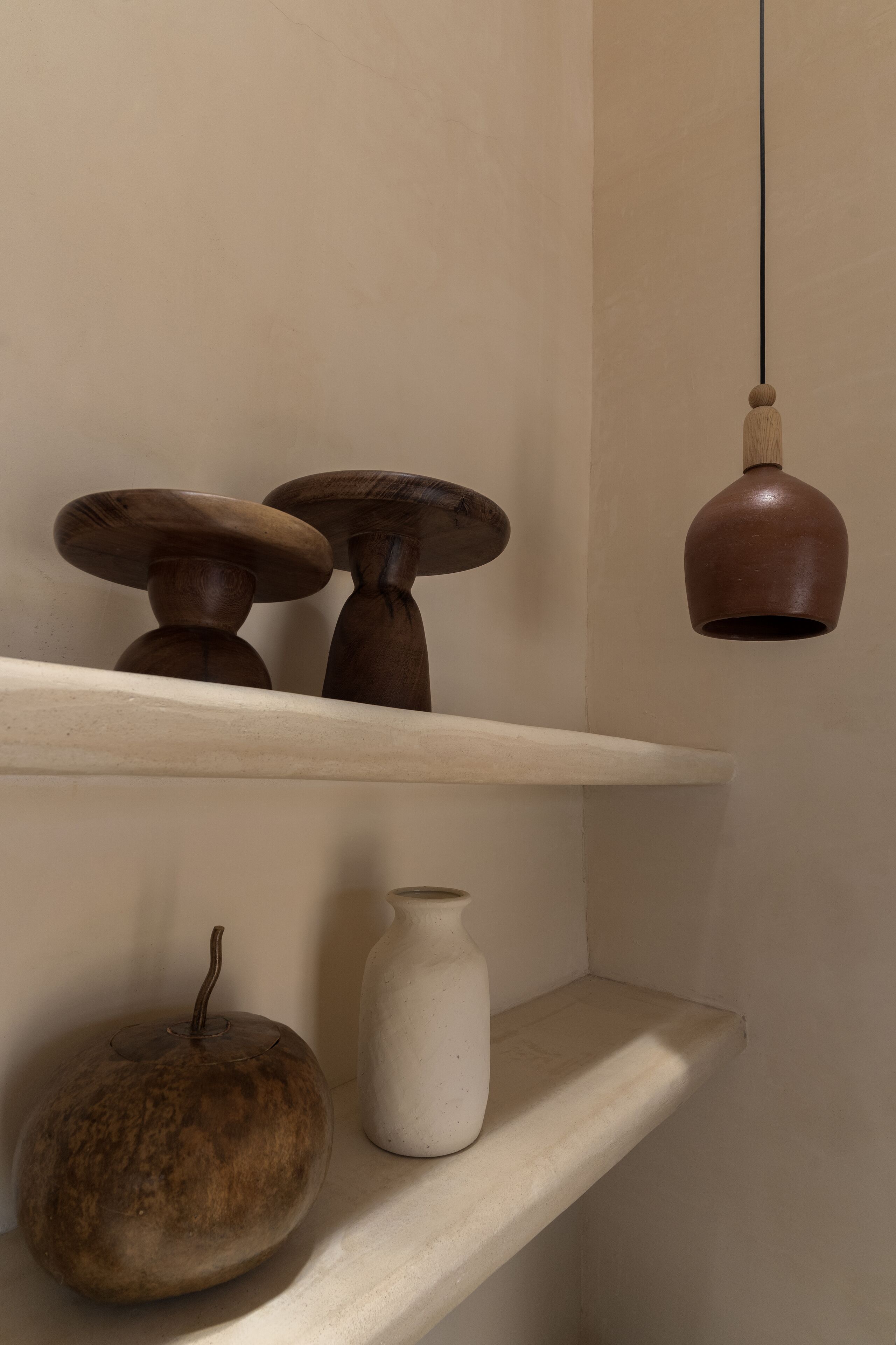 A shelf with a rustic wooden bowl, a white vase, and a hanging light fixture.