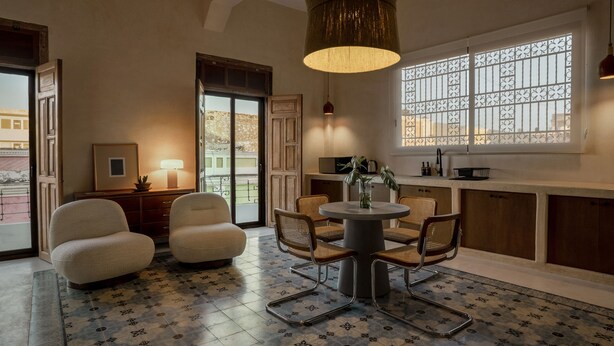 A cozy room with a round table and chairs, a large window with decorative grille, and a hanging lamp. - Narrativ Lofts -Numen- Stylish Hideaway (Campeche)