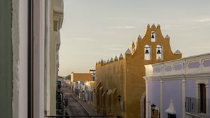 A balcony with a view of a street lined with buildings, including a yellow building with a bell tower. - Narrativ Lofts -Numen- Stylish Hideaway (Campeche)