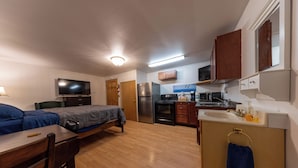 A compact room with a bed, desk, and kitchenette. - Bear Paw Inn (Dillingham)