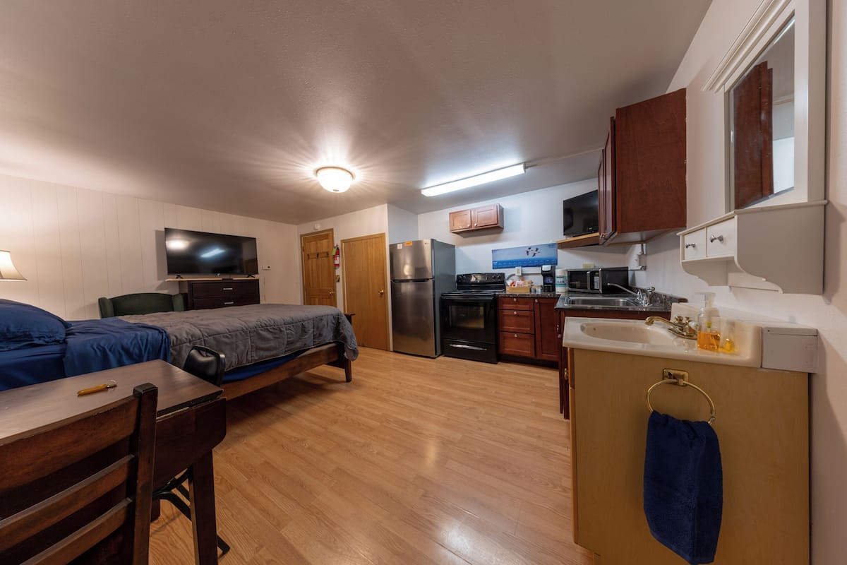 A compact room with a bed, desk, and kitchenette.