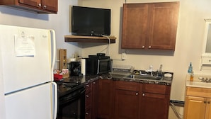 A compact kitchen with wooden cabinets, a refrigerator, stove, microwave, and a television above the counter. - Bear Paw Inn (Dillingham)