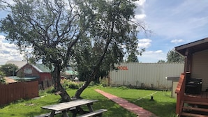 A backyard with a picnic table, a white plastic chair, a wooden deck, and a corrugated metal container. - Bear Paw Inn (Dillingham)