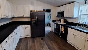 A kitchen with white cabinets, a black refrigerator, and a wooden floor. - 50 acre homestead to hike, forage, harvest, explore, & ENJOY! (Sistersville)