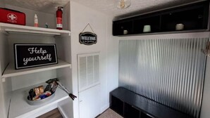 A home office with a white desk, shelves with various items, a 'Help yourself' sign, a 'Welcome' sign, and a black bench. - 50 acre homestead to hike, forage, harvest, explore, & ENJOY! (Sistersville)